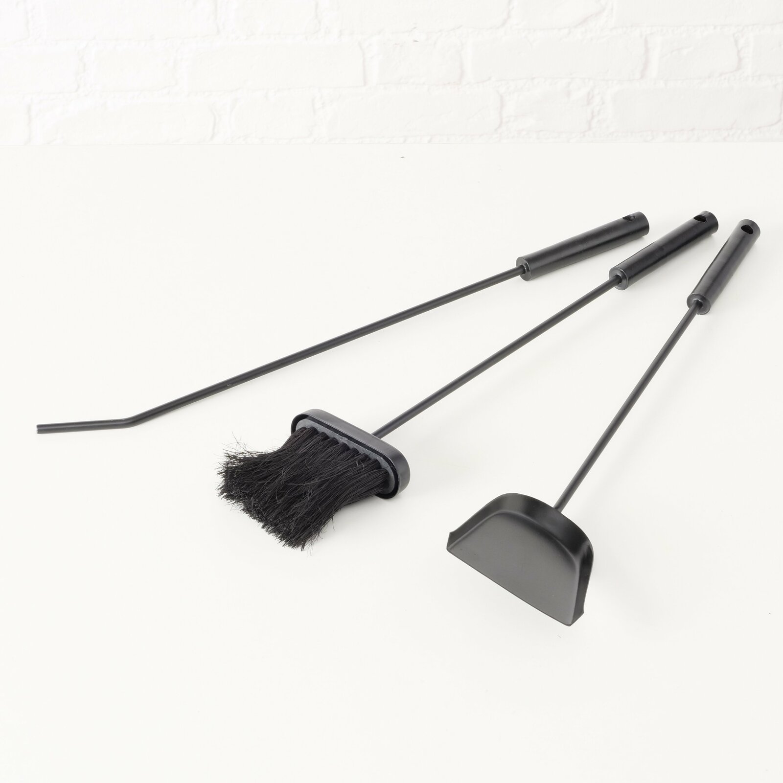 Kaminbesteck Mika, 4-teilig, bestehend aus Schaufel, Besen und Schürhaken, in schwarzer Farbe, auf weißem Hintergrund liegend, seitliche Perspektive.