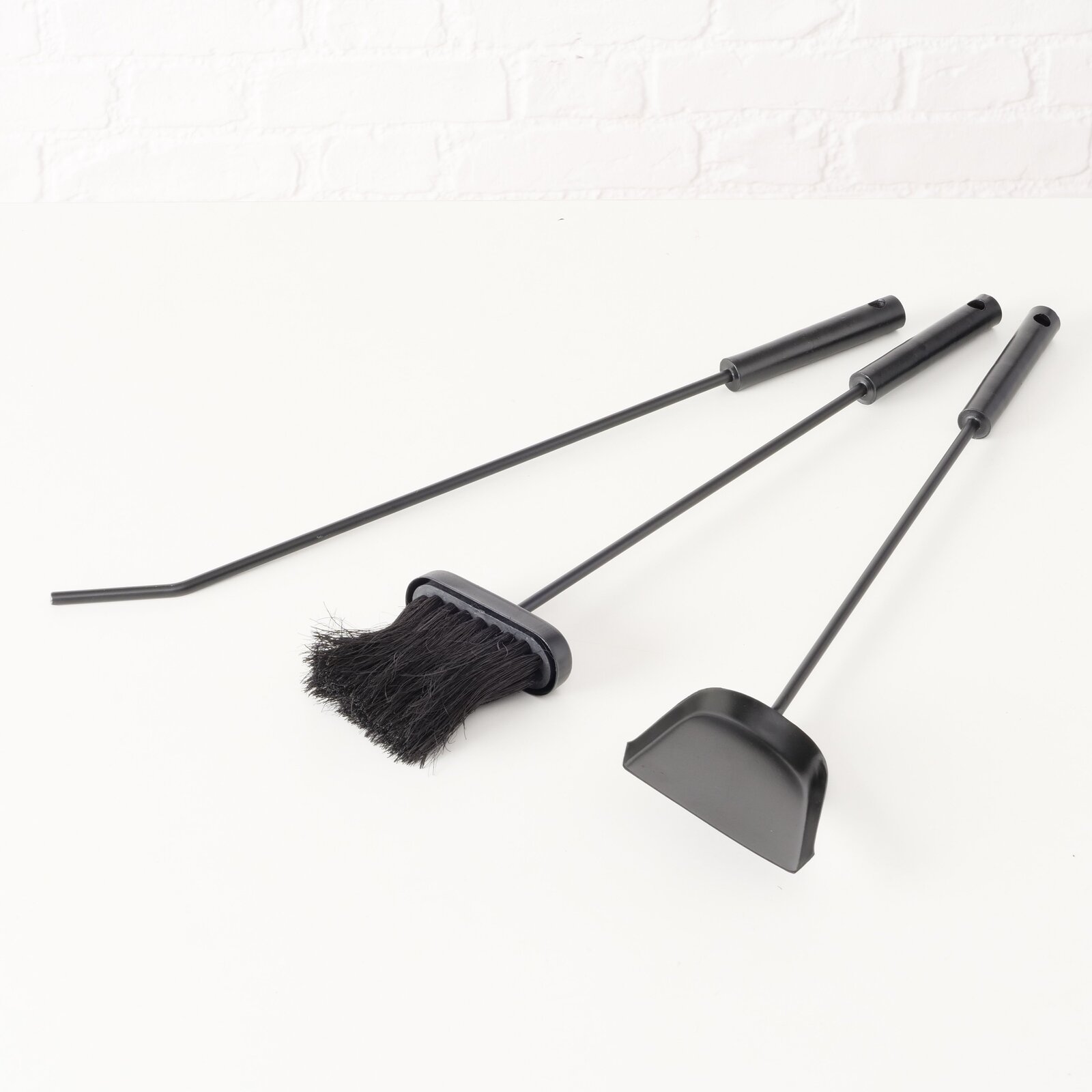 Kaminbesteck Mika, 4-teilig, bestehend aus Schaufel, Besen und Schürhaken, in schwarzer Farbe, auf weißem Hintergrund liegend, seitliche Perspektive.