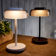 Zwei LED Tischleuchten in modernem Design, eine in Weiß und eine in Schwarz, auf einem Tisch stehend, seitliche Perspektive.