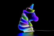 Bunte LED-Lampe in Einhornform mit regenbogenfarbenem Leuchteffekt auf weißem Sockel und Kabel vor schwarzem Hintergrund, seitliche Ansicht