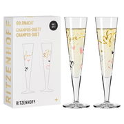 Zwei elegante Champagnergläser mit goldenen und bunten Herzmotiven, präsentiert in einer stilvollen Verpackung mit der Aufschrift 'Goldnacht Champus-Duett'. Frontale Ansicht.