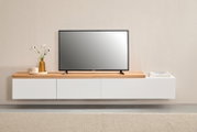 Modernes, schwebendes TV-Lowboard in Weiß mit Holzoberfläche, darauf ein Flachbildfernseher sowie Vase und Bücher; Frontalansicht auf Augenhöhe.