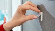 Nahaufnahme einer Hand, die einen tesa Powerstrip Waterproof an einer Wand befestigt.