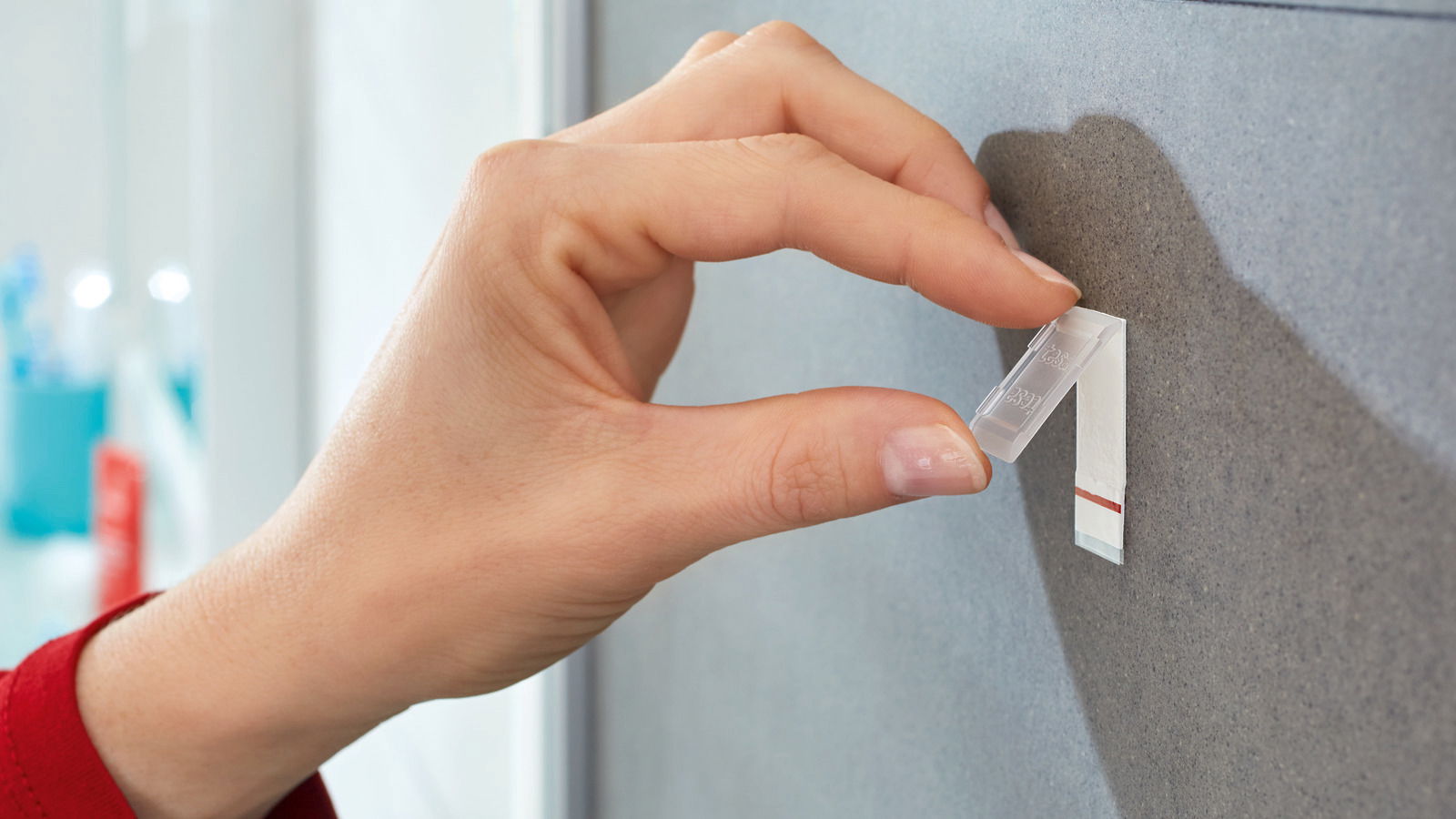 Nahaufnahme einer Hand, die einen tesa Powerstrip Waterproof an einer Wand befestigt.