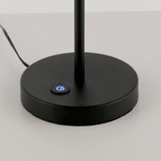 Schwarzer runder Lampenfuß einer Tischlampe mit blau beleuchtetem Ein-/Aus-Touchknopf und sichtbarem Kabel, Nahaufnahme in leichter Draufsicht von vorne