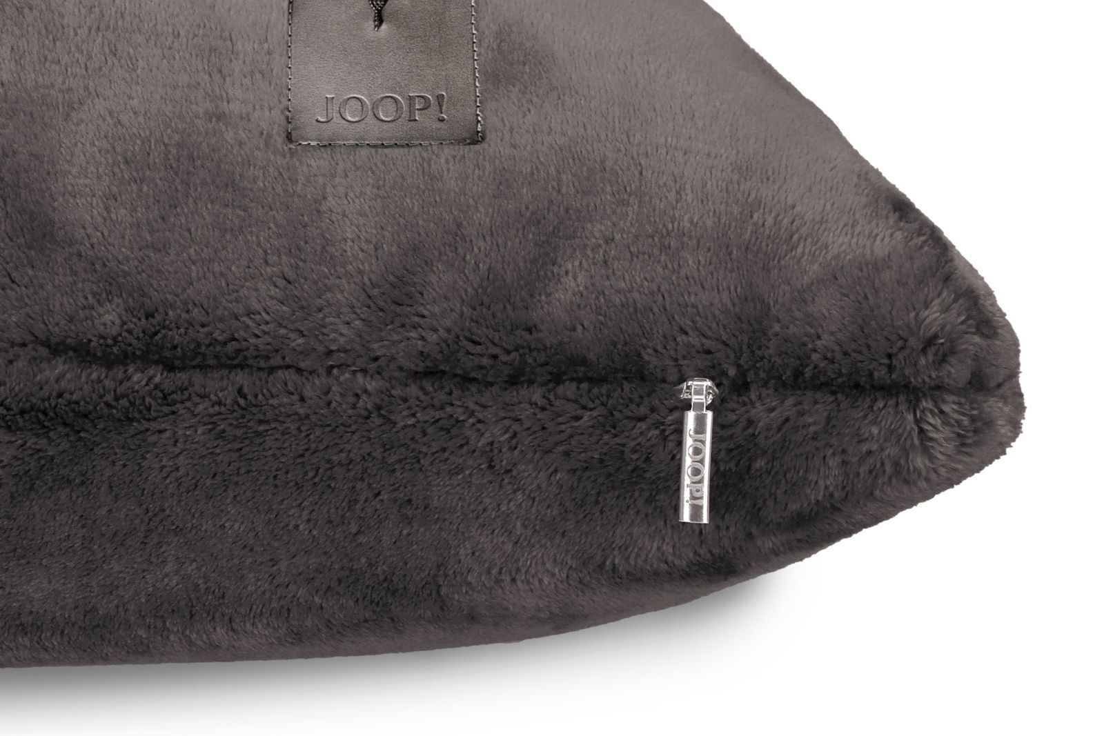 Nahaufnahme einer grauen, flauschigen Kissenhülle mit Reißverschluss und Logo-Detail, seitliche Perspektive