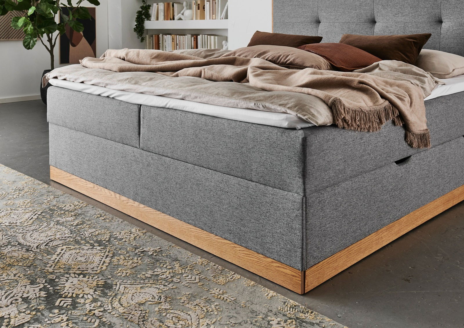 Graues Boxbett mit Holzrahmen, seitliche Perspektive, dekoriert mit Kissen und Decken in einem modernen Schlafzimmer.