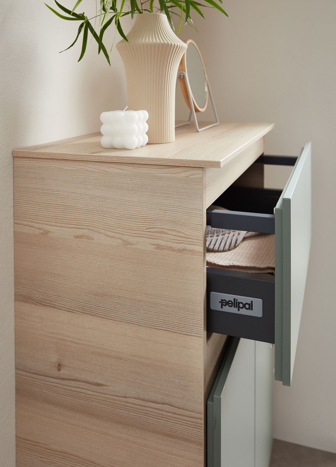 Nahaufnahme eines Unterschranks mit geöffneter Schublade, dekoriert mit einer Vase, einem Spiegel und einer Kerze auf der Abdeckplatte.