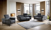 Wohnzimmer mit modernem, grauem Ledersofa-Set bestehend aus einem Dreisitzer, Zweisitzer und Sessel, vor einem Kamin und großen Fenstern mit Stadtblick, aus frontaler Perspektive.