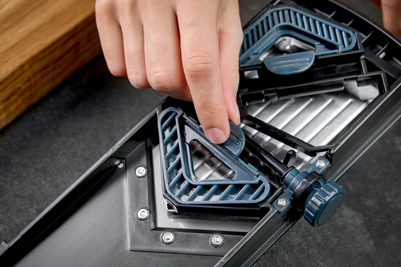 Nahaufnahme eines V-Hobels mit Julienne-Einsatz, von oben betrachtet, während eine Hand den Einsatz justiert.