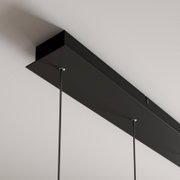 Schwarze, rechteckige Deckenhalterung einer Pendelleuchte mit zwei abgehenden Kabeln, aus schräger Untersicht aufgenommen.