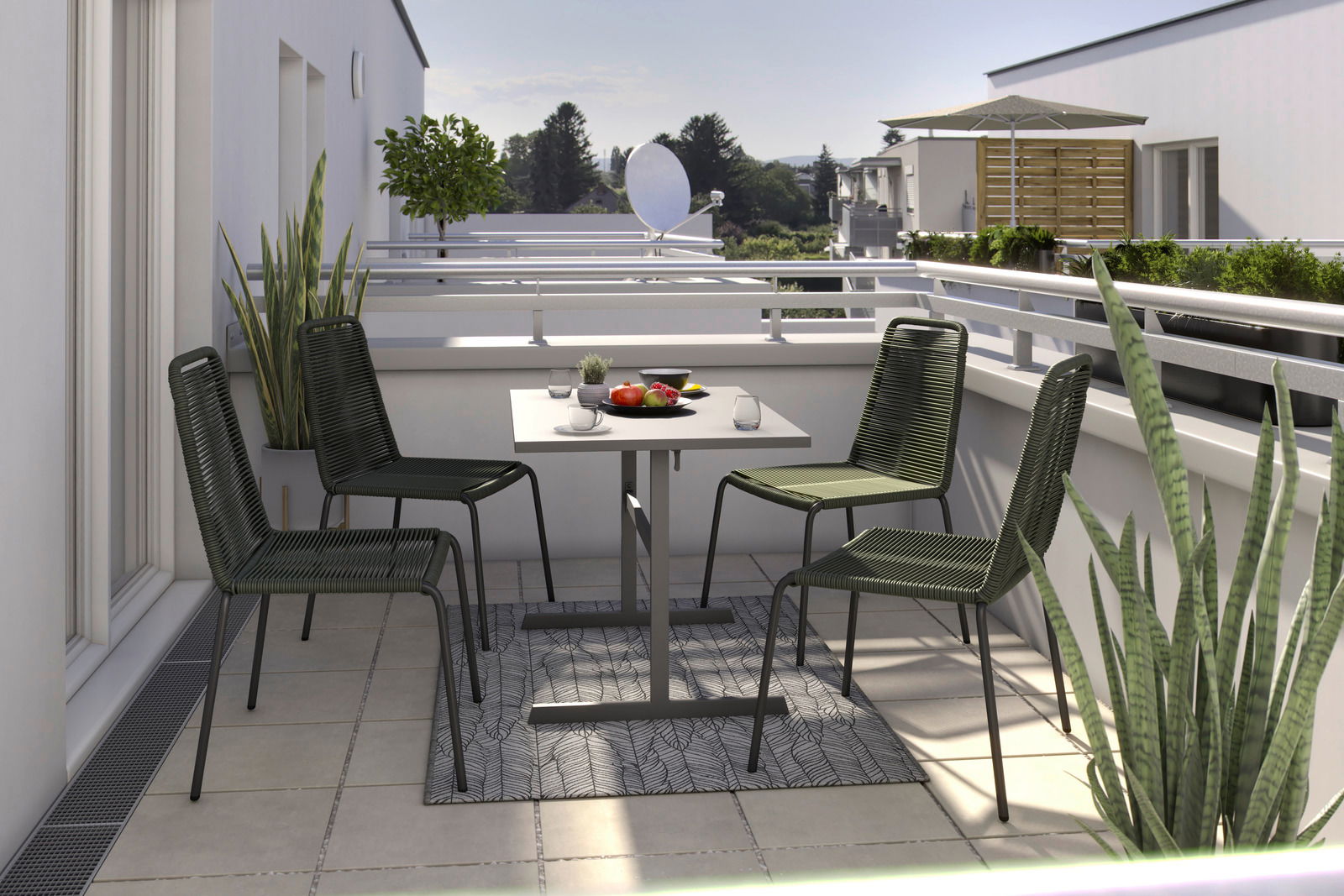 Vier grüne Stapelstühle um einen quadratischen Tisch auf einem Balkon, mit Pflanzen und einer Aussicht auf Bäume im Hintergrund, aus einer seitlichen Perspektive fotografiert.