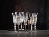 Sechs elegante Sektgläser aus Kristall mit feinem Schliff, teilweise gefüllt mit Sekt, auf einem Tisch vor dunklem Hintergrund, seitliche Perspektive.