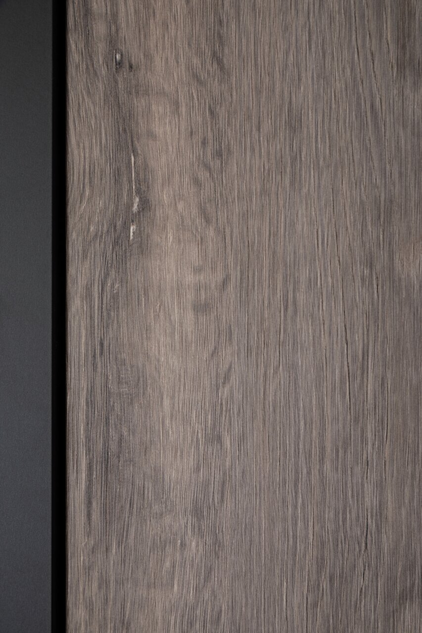 Nahaufnahme einer Holzoberfläche mit natürlicher Maserung und einem schwarzen Rand auf der linken Seite.