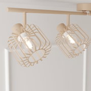 Beige Deckenleuchte mit zwei schwenkbaren Spotköpfen und geometrischen Drahtkäfig-Schirmen, aufgenommen aus leicht schräger Untersicht in einem hellen Raum