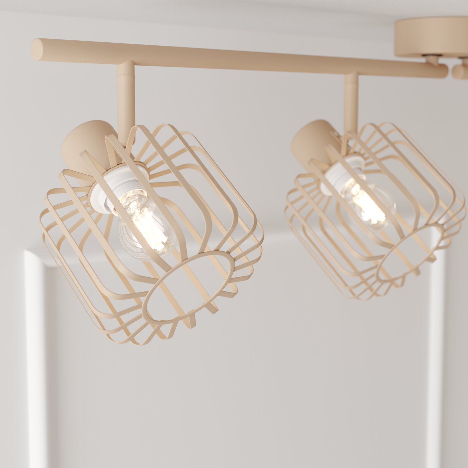 Beige Deckenleuchte mit zwei schwenkbaren Spotköpfen und geometrischen Drahtkäfig-Schirmen, aufgenommen aus leicht schräger Untersicht in einem hellen Raum