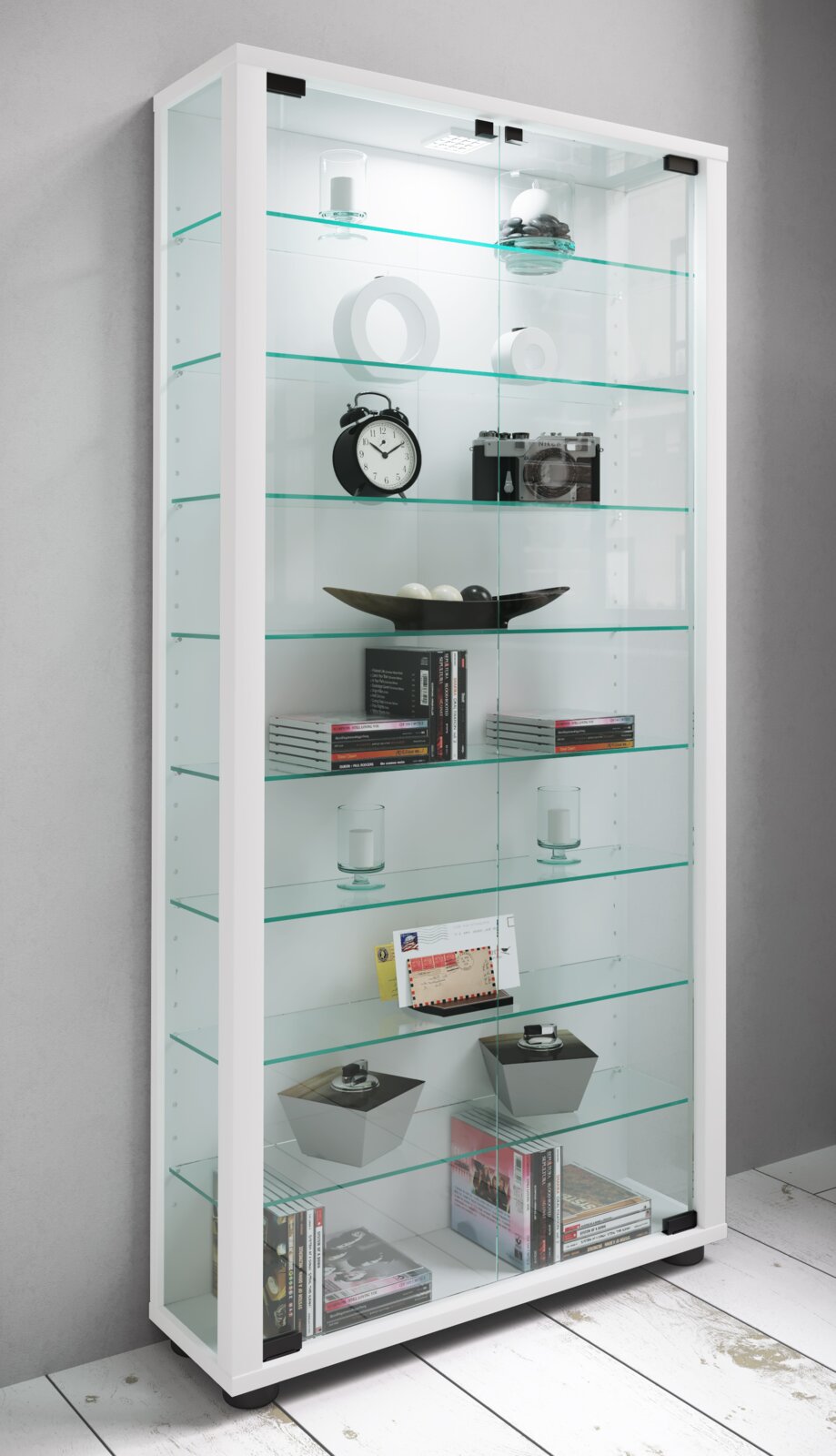 Weiße Glasvitrine mit LED-Beleuchtung und mehreren Glasböden, gefüllt mit Deko und Büchern, aus schräger Vorderansicht (leicht von links)