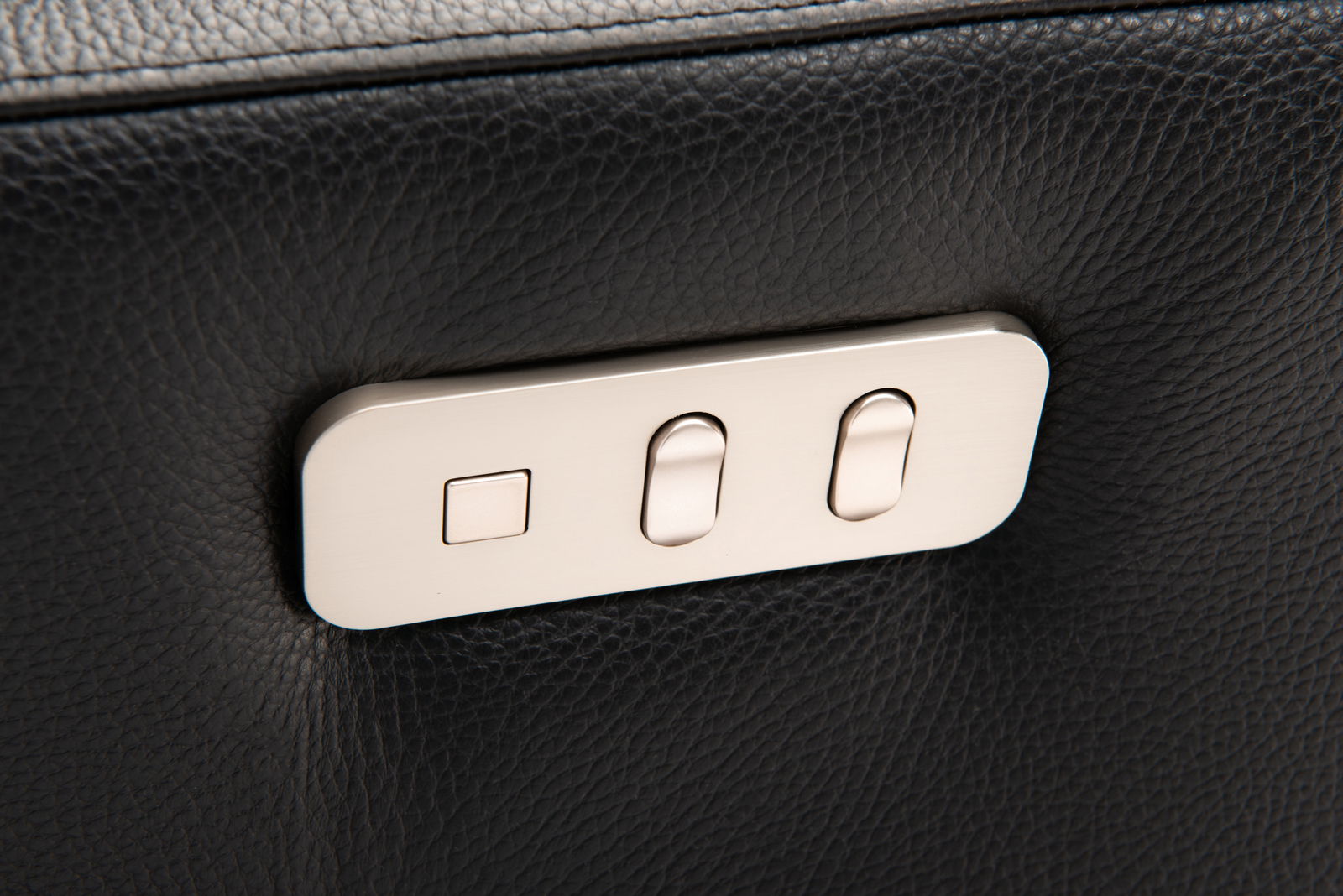 Nahaufnahme der Bedienelemente eines Relaxsessels aus schwarzem Leder mit silbernen Knöpfen.