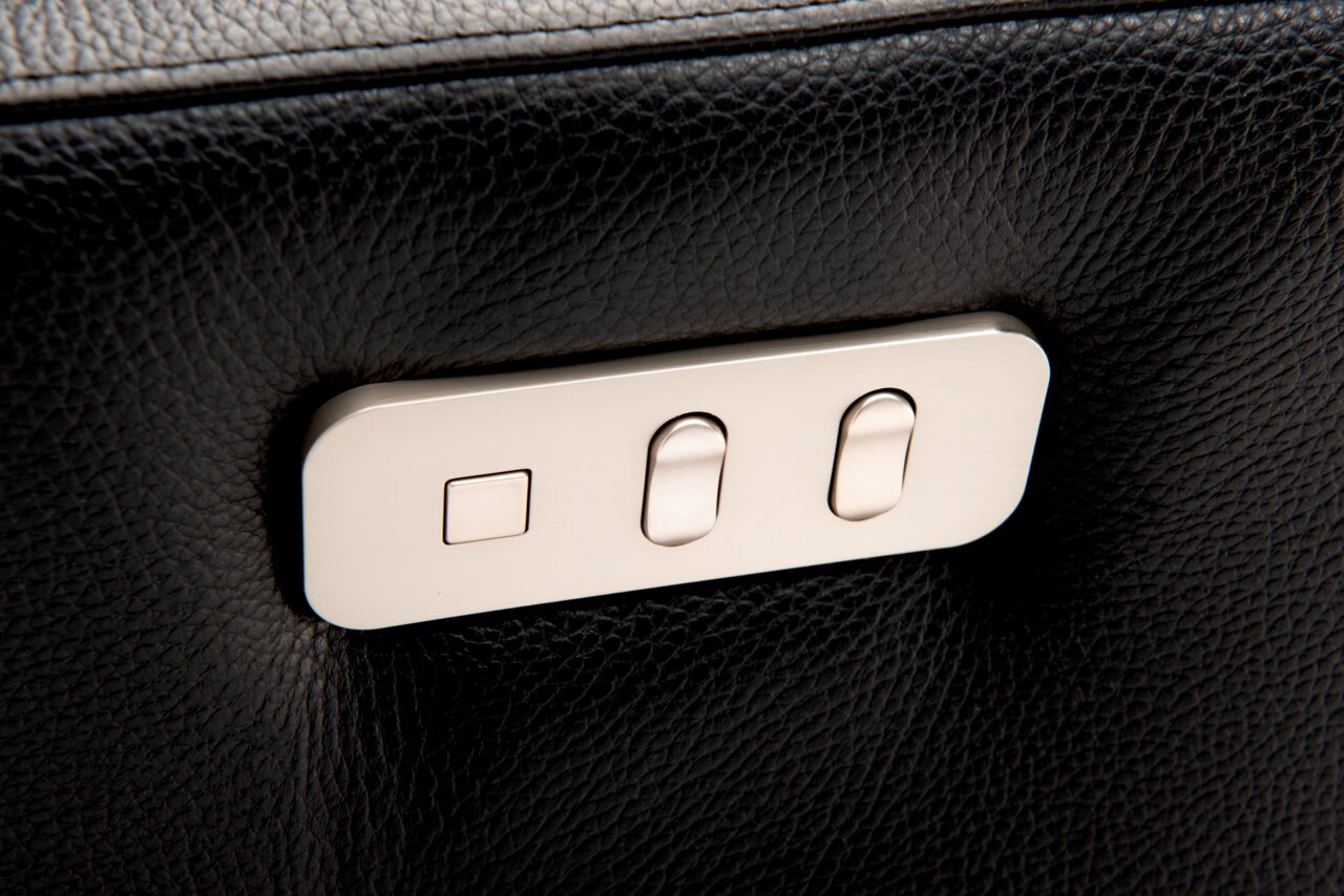 Close-up van de bedieningselementen van een relaxfauteuil van zwart leer met zilveren knoppen.