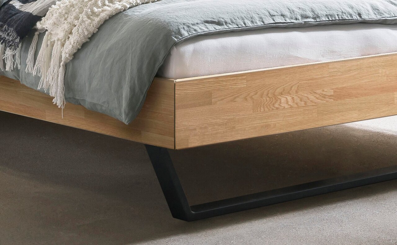 Close-up van een modern houten bedframe met een zwart metalen onderstel, gezien vanaf de zijkant.