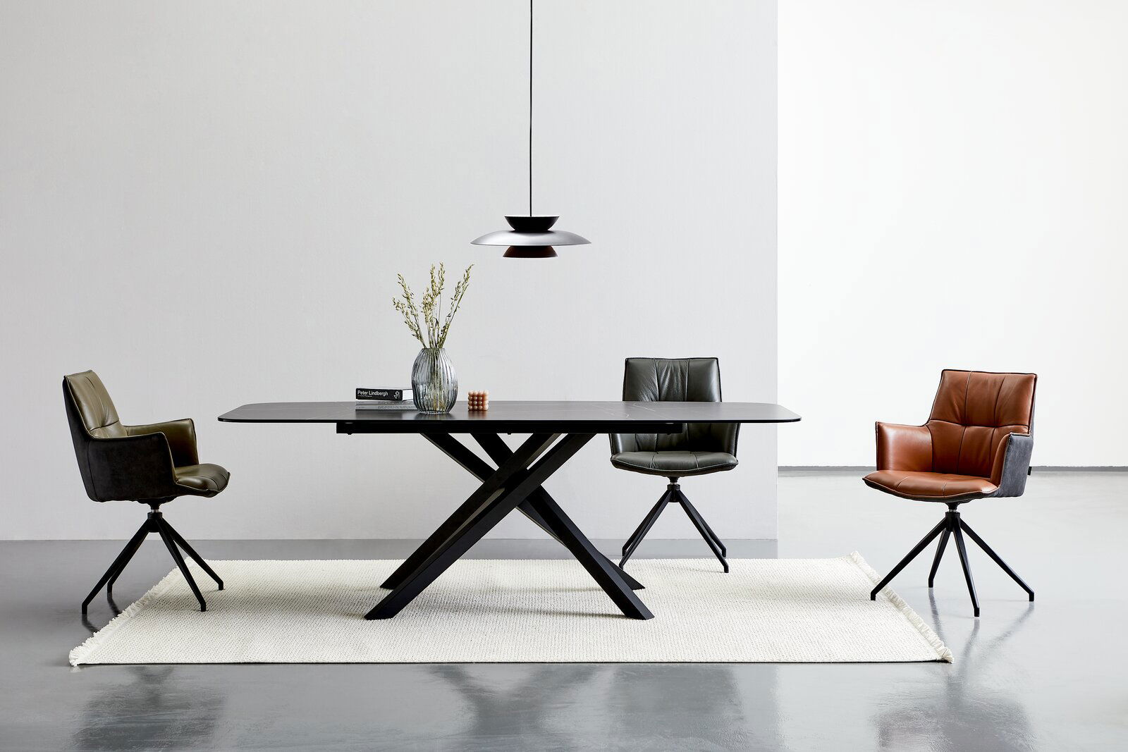 Novel Esstisch UFO Moderner Esstisch mit schwarzer Tischplatte und X-förmigem Gestell, umgeben von drei stilvollen Stühlen in verschiedenen Farben, aus der Frontalperspektive.