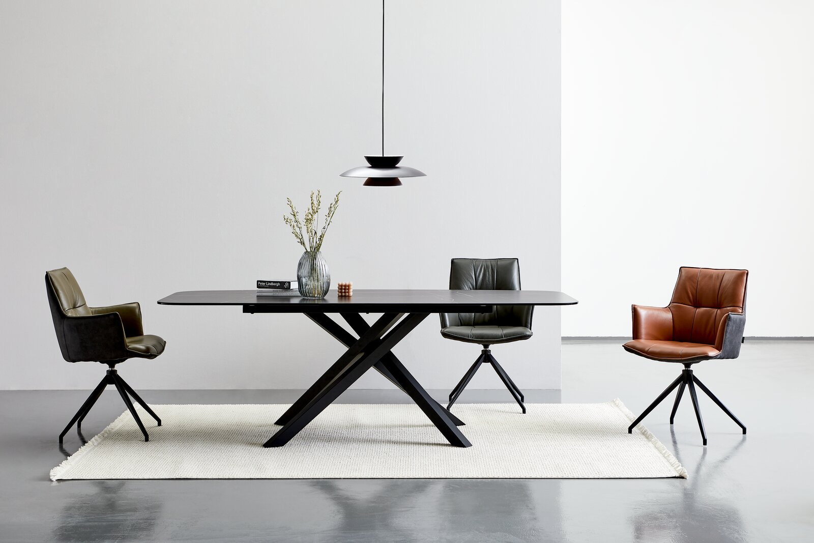 Novel Esstisch UFO Moderner Esstisch mit schwarzer Tischplatte und X-förmigem Gestell, umgeben von drei stilvollen Stühlen in verschiedenen Farben, aus der Frontalperspektive.