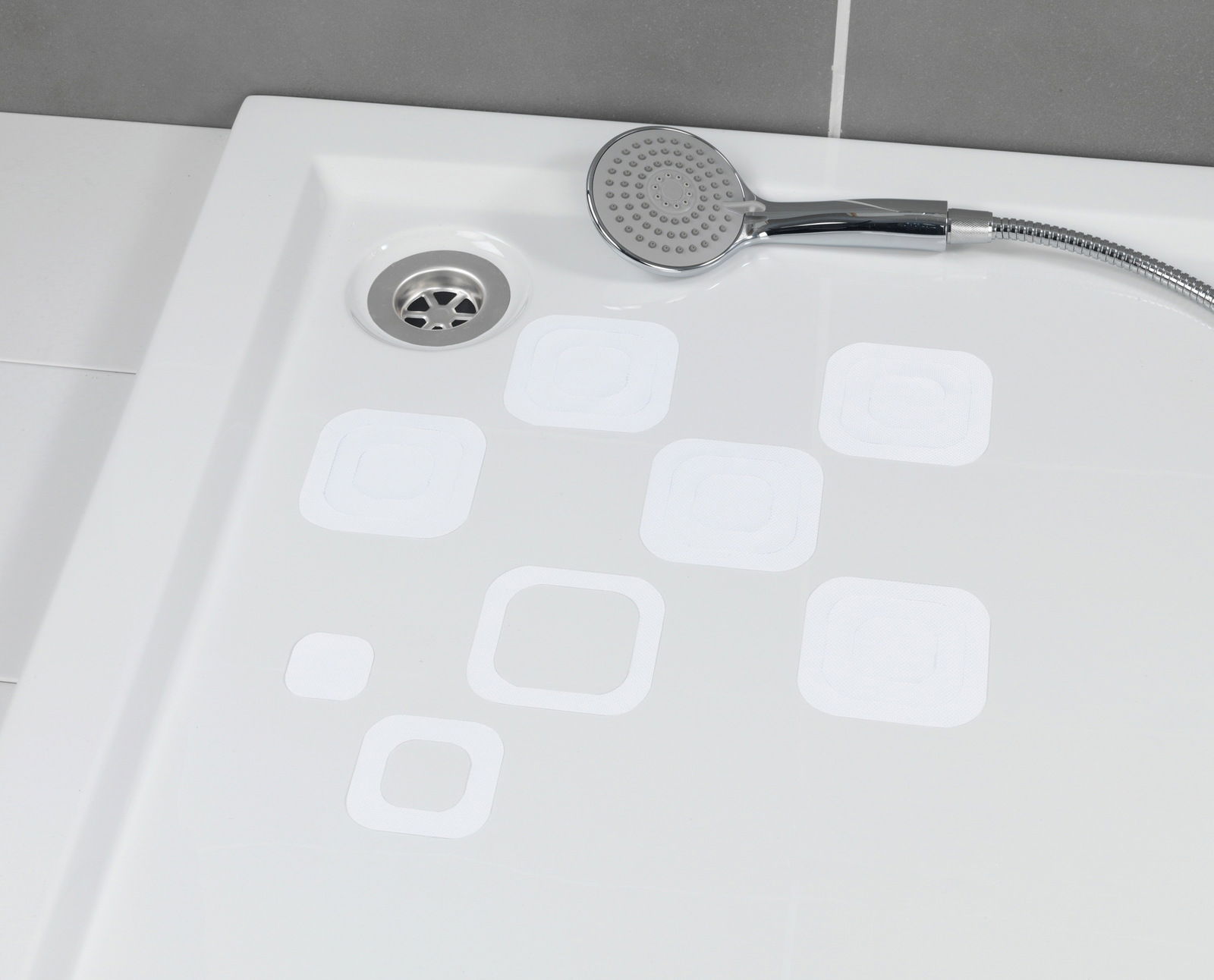 Blick von oben auf eine Duschwanne mit weißen, eckigen Anti-Rutschstickern und einer Handbrause.