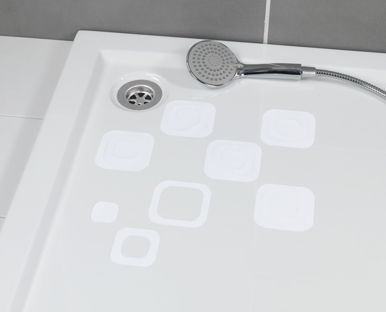 Blick von oben auf eine Duschwanne mit weißen, eckigen Anti-Rutschstickern und einer Handbrause.