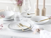 Elegant gedeckter Esstisch mit weißem geriffeltem Geschirr, goldfarbenem Besteck und Glaswaren, fotografiert aus leicht erhöhter, schräger Perspektive von vorne.