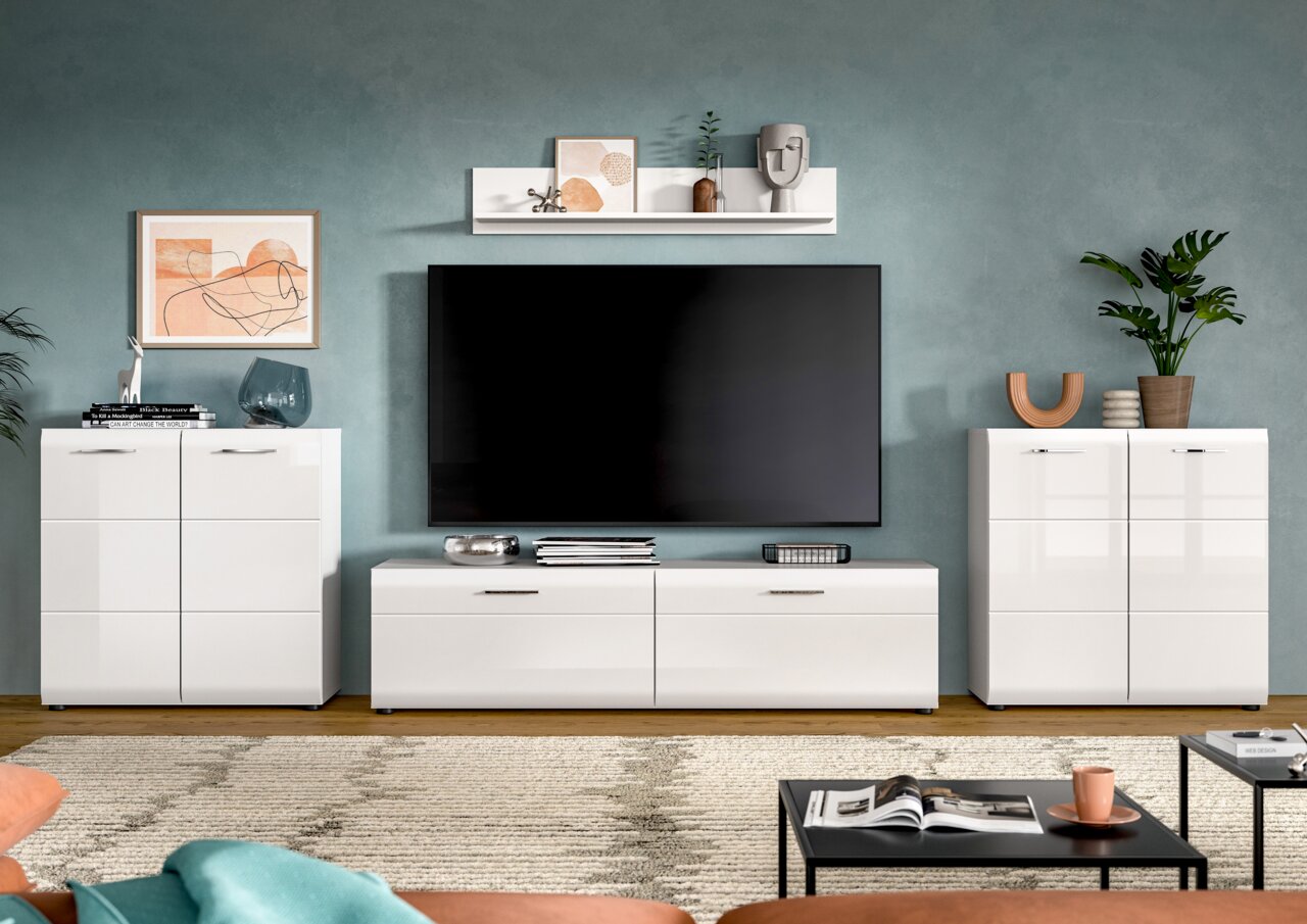 Modernes Wohnzimmer-Setup mit weißer TV-Wandmöbel-Kombination (Lowboard und zwei Highboards) und großem Flachbildfernseher, frontal aus Augenhöhe fotografiert.