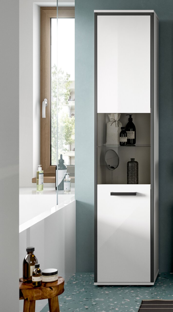 Hoher, schmaler Badezimmer-Hochschrank in Weiß mit schwarzem Rahmen, oben Spiegeltür, mittig offene Ablage mit Pflegeprodukten und unten Schublade; frontale Ansicht in einem modernen Bad neben Badewanne und Fenster.