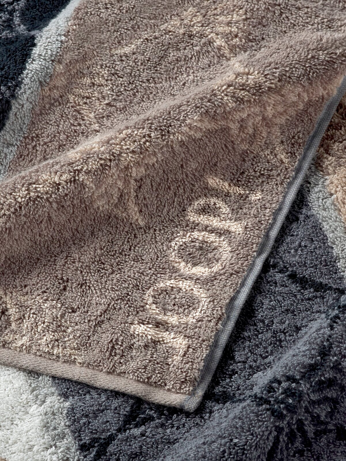 JOOP! Handtuch SIGNATURE Nahaufnahme eines JOOP! Handtuchs aus der SIGNATURE Kollektion in verschiedenen Grautönen, das gefaltet auf einer Oberfläche liegt.