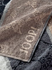 Close-up van een JOOP!-handdoek uit de SIGNATURE-collectie in verschillende grijstinten, die opgevouwen op een oppervlak ligt.
