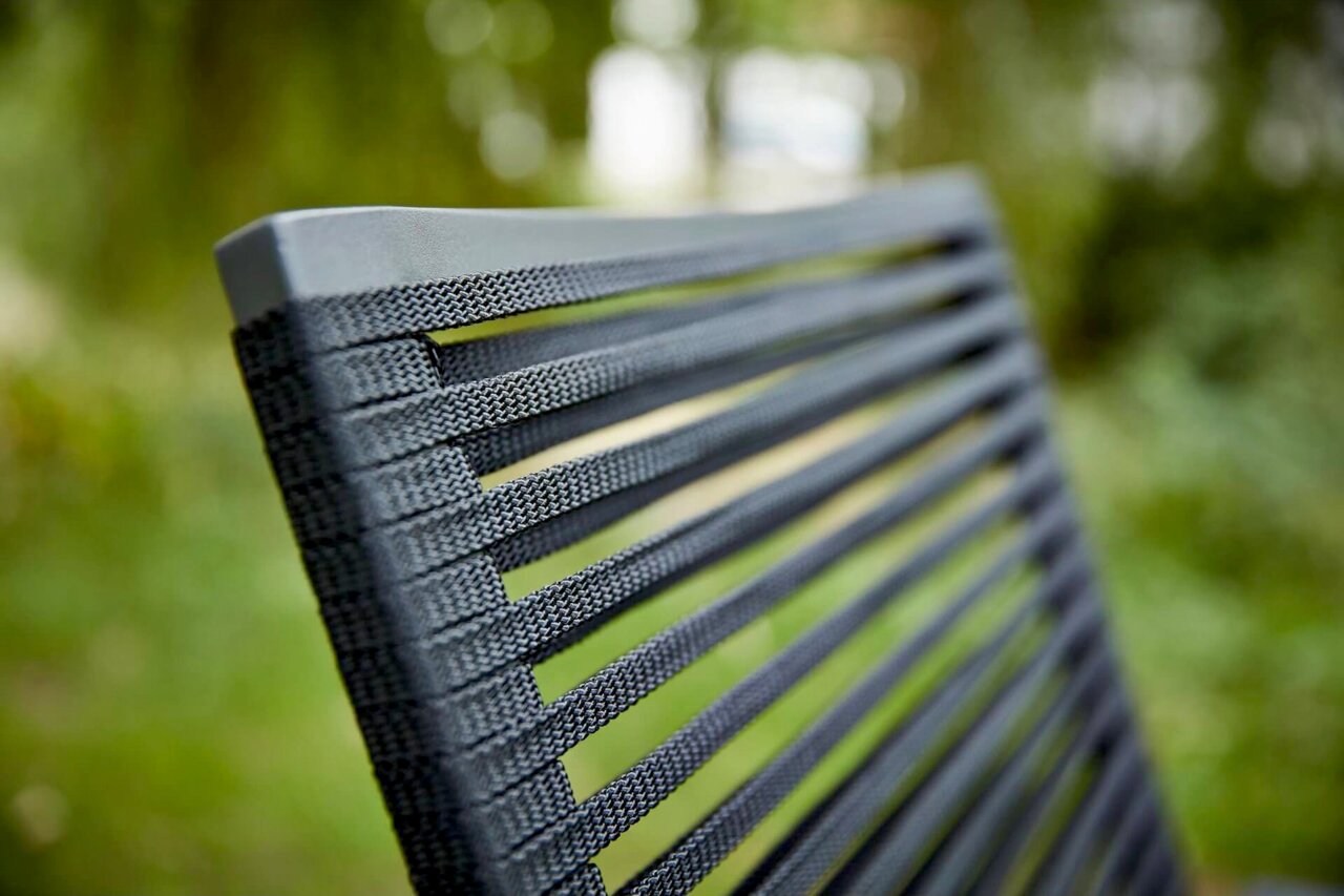 Nahaufnahme der Rückenlehne eines Sessels mit grauen, gewebten Streifen, im Freien fotografiert.