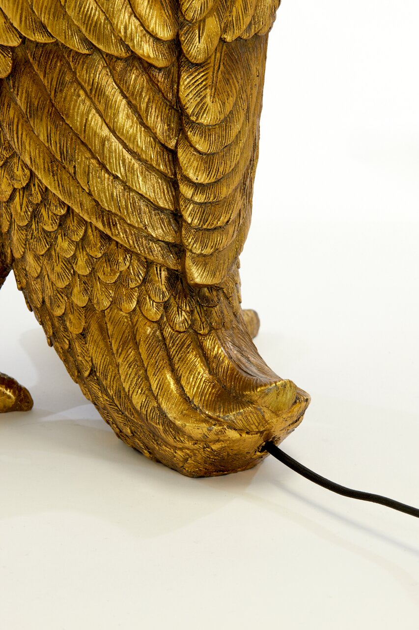 Close-up van een gouden tafellamp in de vorm van een vogel met gedetailleerde veren, gezien vanuit de zijkant.
