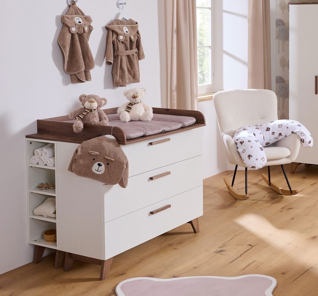 Wickelkommode aus Holz mit drei Schubladen, seitlichen Regalfächern und Wickelauflage, im Kinderzimmer mit Teddybären und Babyaccessoires, seitliche Perspektive