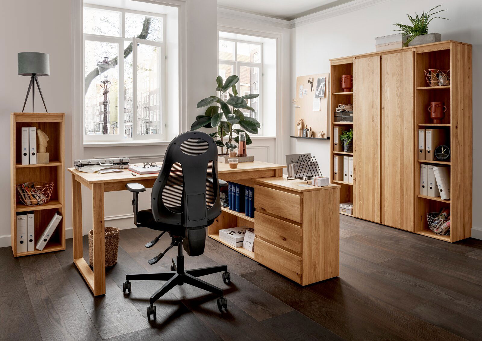 Linea Natura Aktenschrank DURABLE OFFICE Moderne Büromöbelkombination aus Holz mit Eckschreibtisch, Rollcontainer und Aktenschränken in einem hellen Raum mit großen Fenstern, von vorne betrachtet.