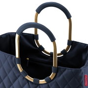 Close-up van een donkerblauwe tas met een doorgestikt ruitpatroon en gouden, ovale handvatten met blauwe details, gezien van bovenaf.