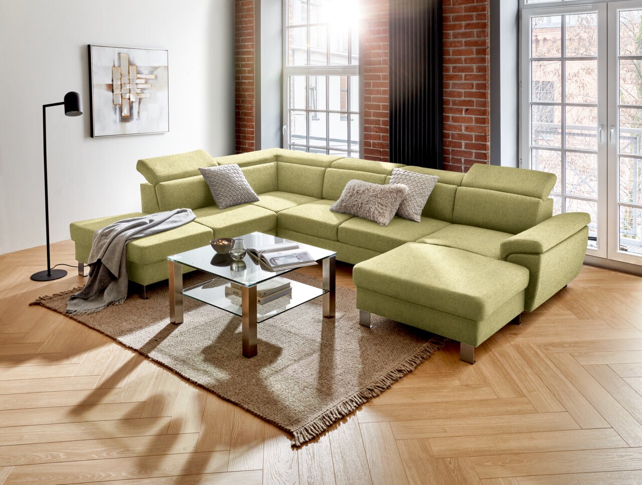 Groene hoekbank (U) in een moderne woonkamer met grote ramen, een houten vloer en een glazen tafel, gezien vanuit het perspectief linksvoor.