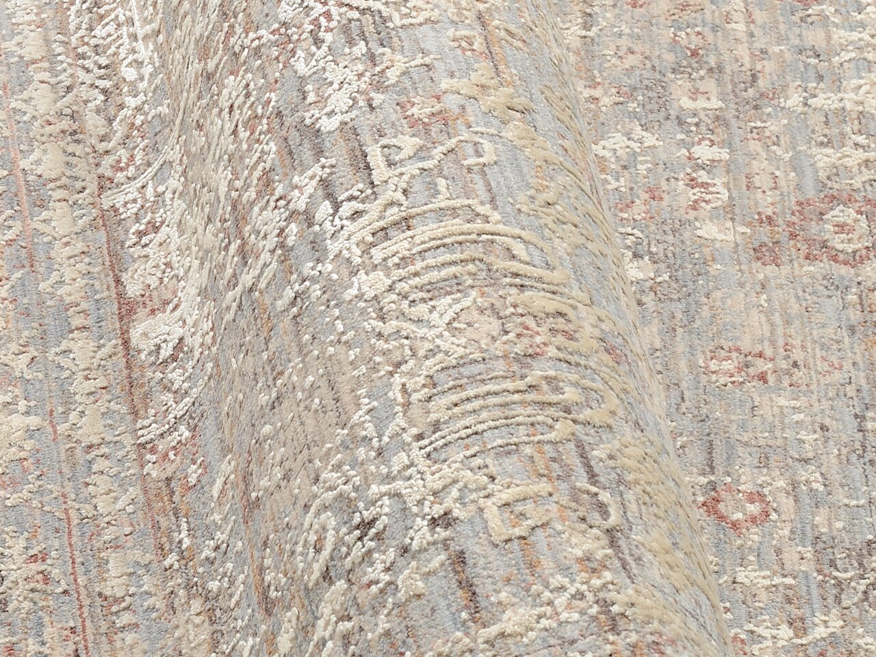 Nahaufnahme eines Designer-Teppichs mit detailliertem Muster in Beige- und Grautönen, aus seitlicher Perspektive aufgenommen.