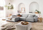 Moderne graue Rundecke in einem hellen Wohnzimmer mit großen Fenstern, Pflanzen und stilvollen Dekorationen, aus der Perspektive von vorne links.