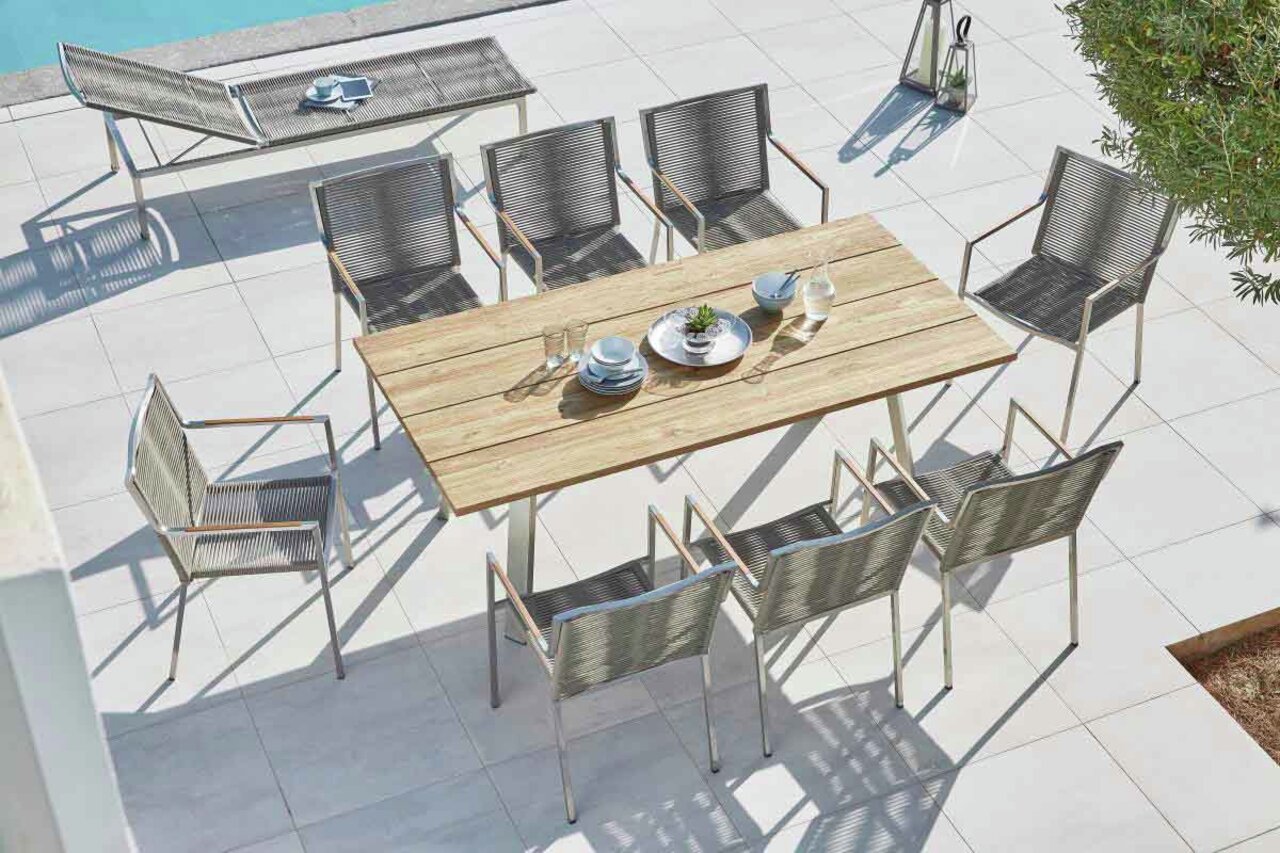 Gartentisch mit Holzplatte und acht Stühlen, aus der Vogelperspektive fotografiert, auf einer Terrasse neben einem Pool.