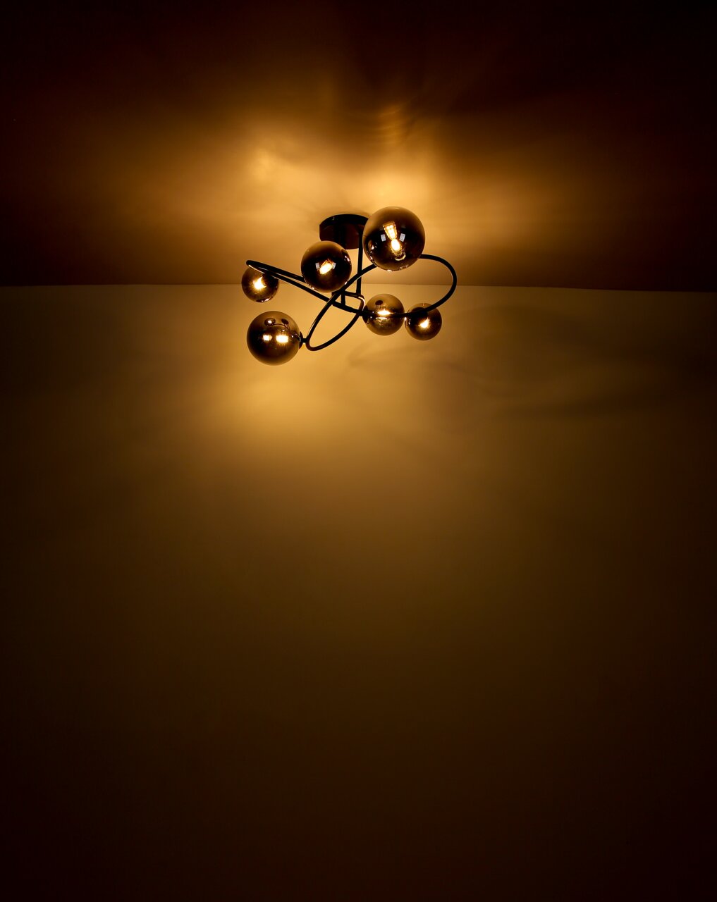 Moderne Deckenleuchte mit mehreren kugelförmigen Leuchtkörpern, die warmes Licht an die Decke strahlen. Perspektive von unten.