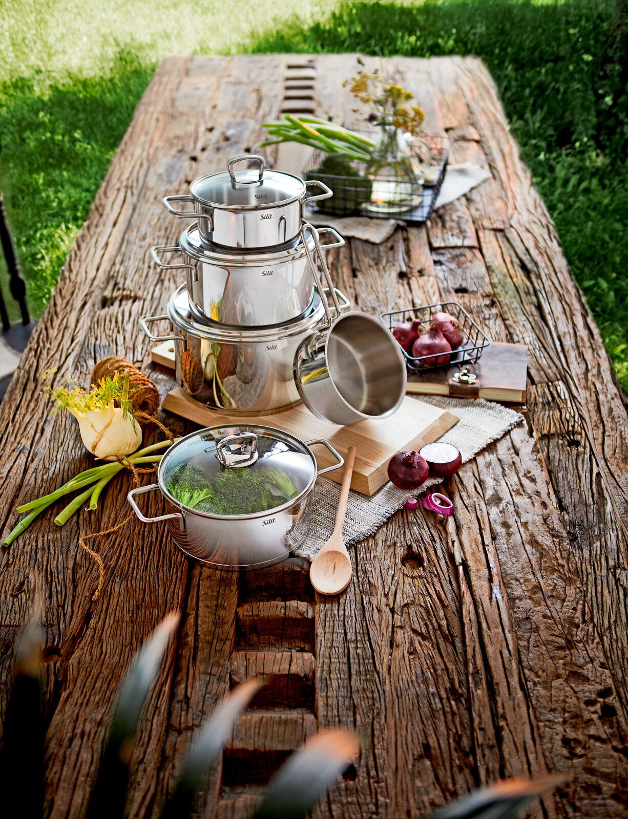 Topfset Alicante 5-tlg aus Edelstahl auf einem rustikalen Holztisch, fotografiert aus der Vogelperspektive, umgeben von frischen Zutaten und Küchenutensilien.
