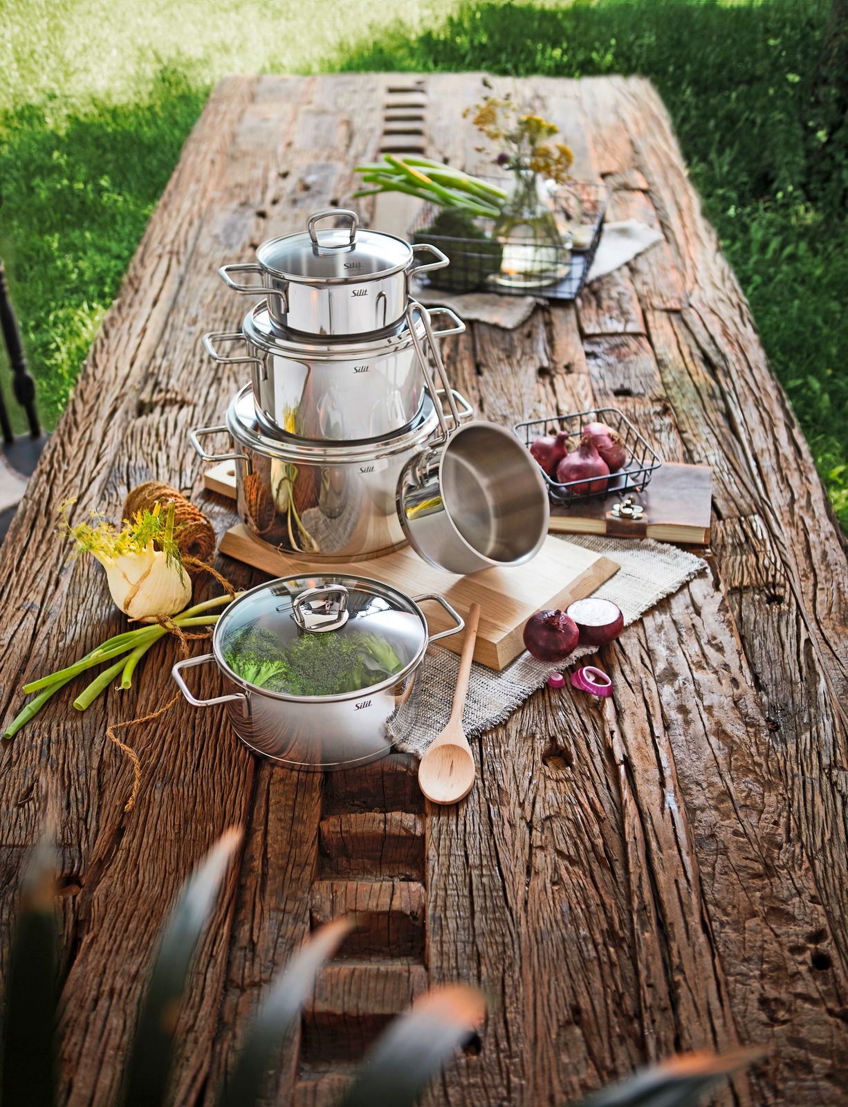 Topfset Alicante 5-tlg aus Edelstahl auf einem rustikalen Holztisch, fotografiert aus der Vogelperspektive, umgeben von frischen Zutaten und Küchenutensilien.