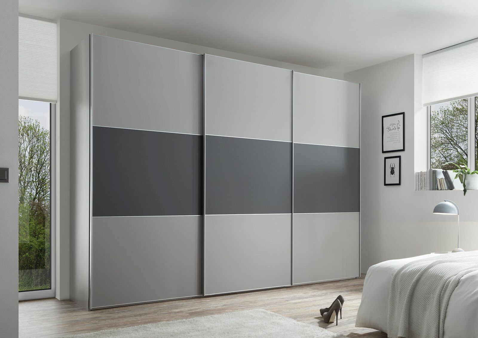 Moderano Schwebetürenschrank PRIMO Moderner Schwebetürenschrank in Grau mit drei Türen, seitliche Perspektive im Schlafzimmer.