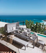 Elegantes Dining-Lounge-Set auf einer Terrasse mit Meerblick, bestehend aus grauen Sofas, Tischen und Bänken, umgeben von Pflanzen. Perspektive von oben.