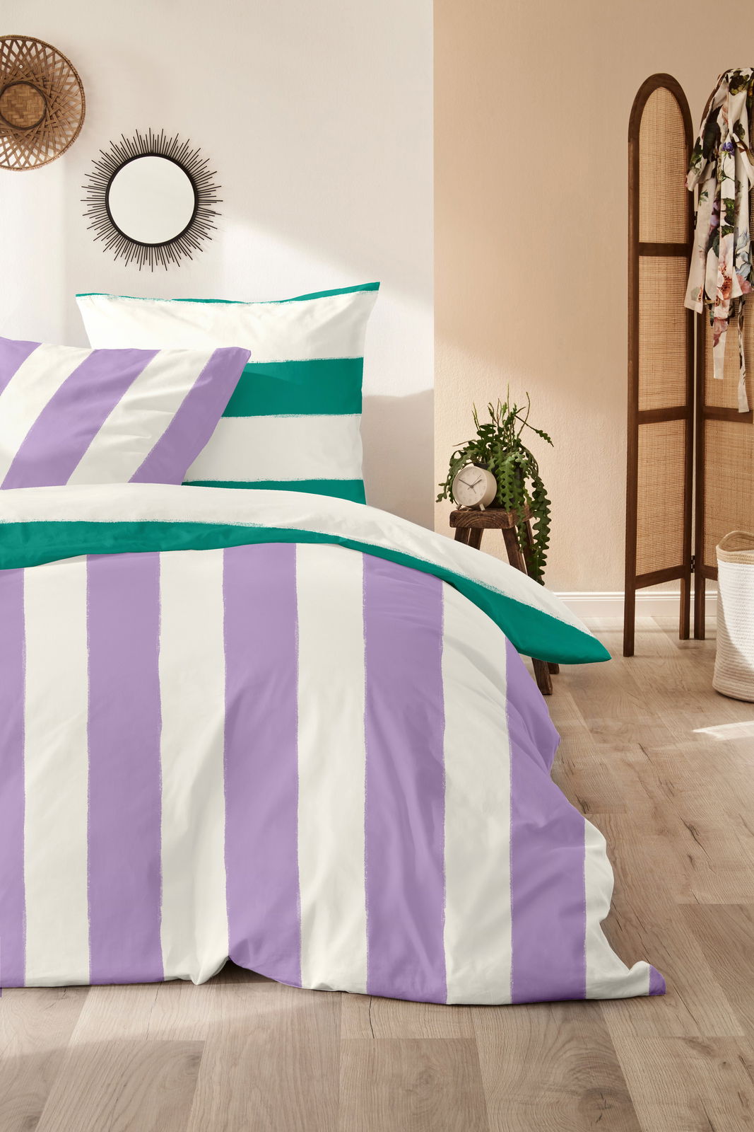 Bettwäsche-Set mit lila und grünen Streifen, fotografiert aus einer seitlichen Perspektive in einem gemütlichen Schlafzimmer.