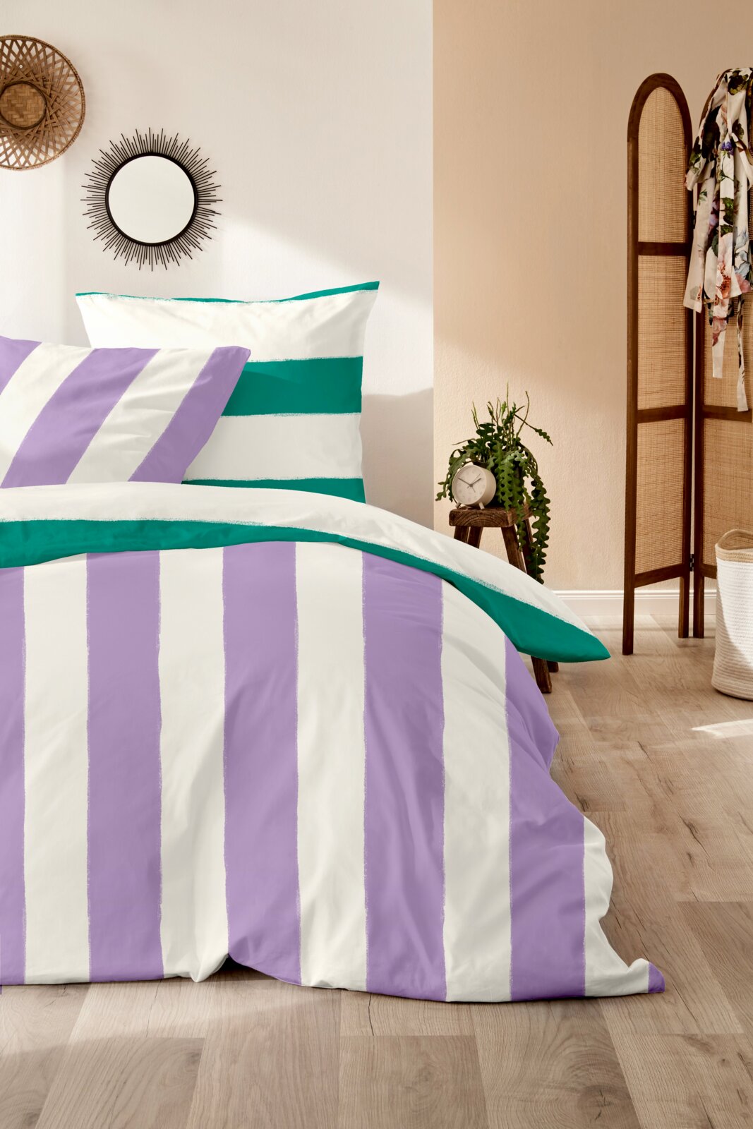 Bettwäsche-Set mit lila und grünen Streifen, fotografiert aus einer seitlichen Perspektive in einem gemütlichen Schlafzimmer.