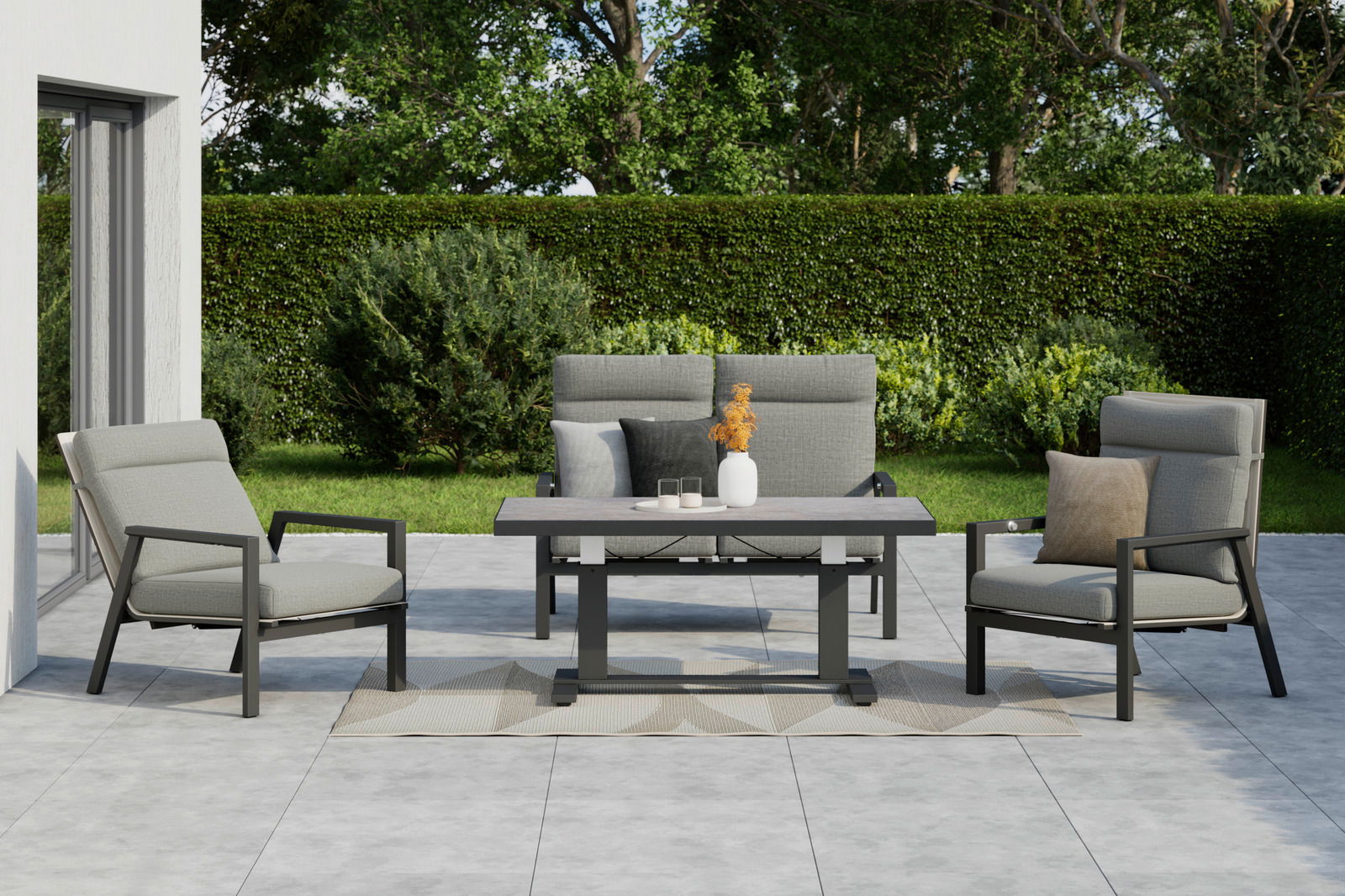 Gartenmöbel-Set mit zwei grauen Sesseln, einer grauen Gartenbank und einem Tisch auf einer Terrasse, umgeben von grüner Hecke und Bäumen, aus frontaler Perspektive.